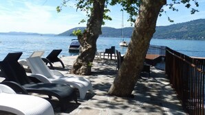 A seaside terrace with lounge chairs, a stone pathway, and a view of the sea and hills. - Hotel Ristorante Beata Giovannina (Verbania)