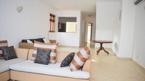 Un salón con un sofá color beige, cojines estampados, una mesa redonda de madera y una pared blanca con una concha decorativa.
