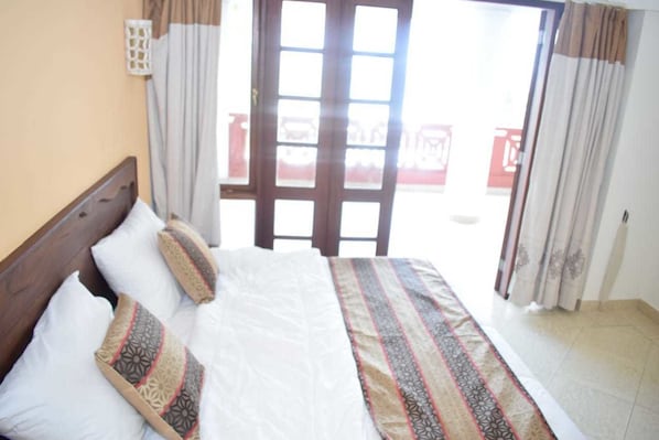 A hotel room with a bed, curtains, and a view through a glass door.