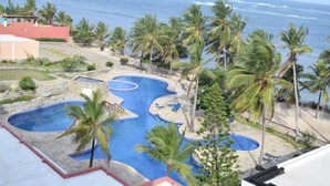 Ein Resort mit großzügigem Poolbereich, umgeben von Palmen und Blick auf den Ozean.