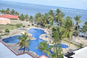 A resort with a large pool area surrounded by palm trees and a view of the ocean.