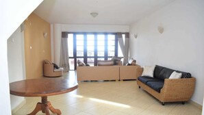Una sala de estar con una mesa redonda de madera, un conjunto de sofás y un ventanal con cortinas.