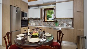 Une cuisine moderne avec des meubles en bois, un réfrigérateur en acier inoxydable, un four à micro-ondes et une table à manger pour deux personnes, agrémentée de verres à vin et d’un panier de fruits.
