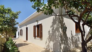 Un bâtiment doté d’une galerie couverte, de volets en bois et d’un arbre qui offre de l’ombre.