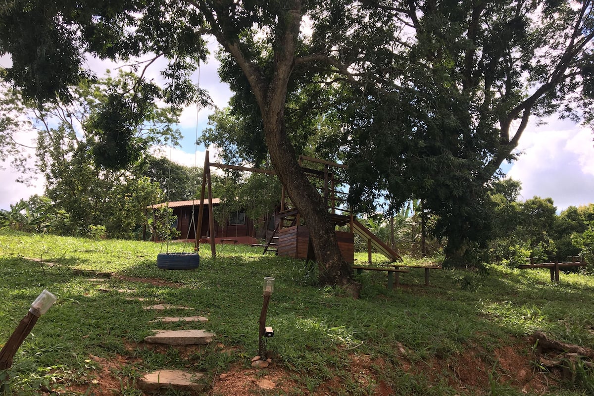 A rustic outdoor area with a wooden swing, a tire swing, and a small wooden structure.