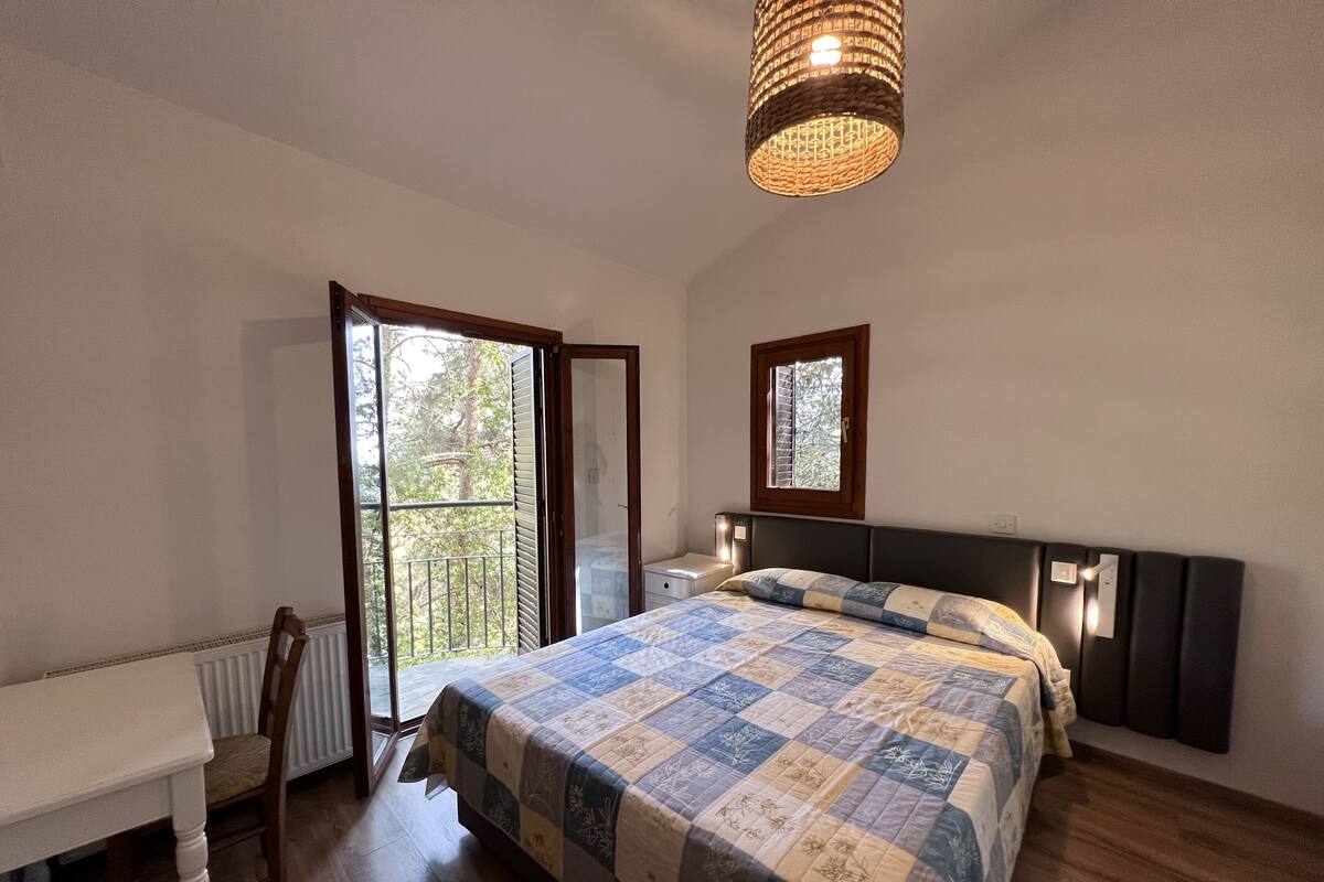 A bedroom with a bed, a desk, a window, and a ceiling light fixture.