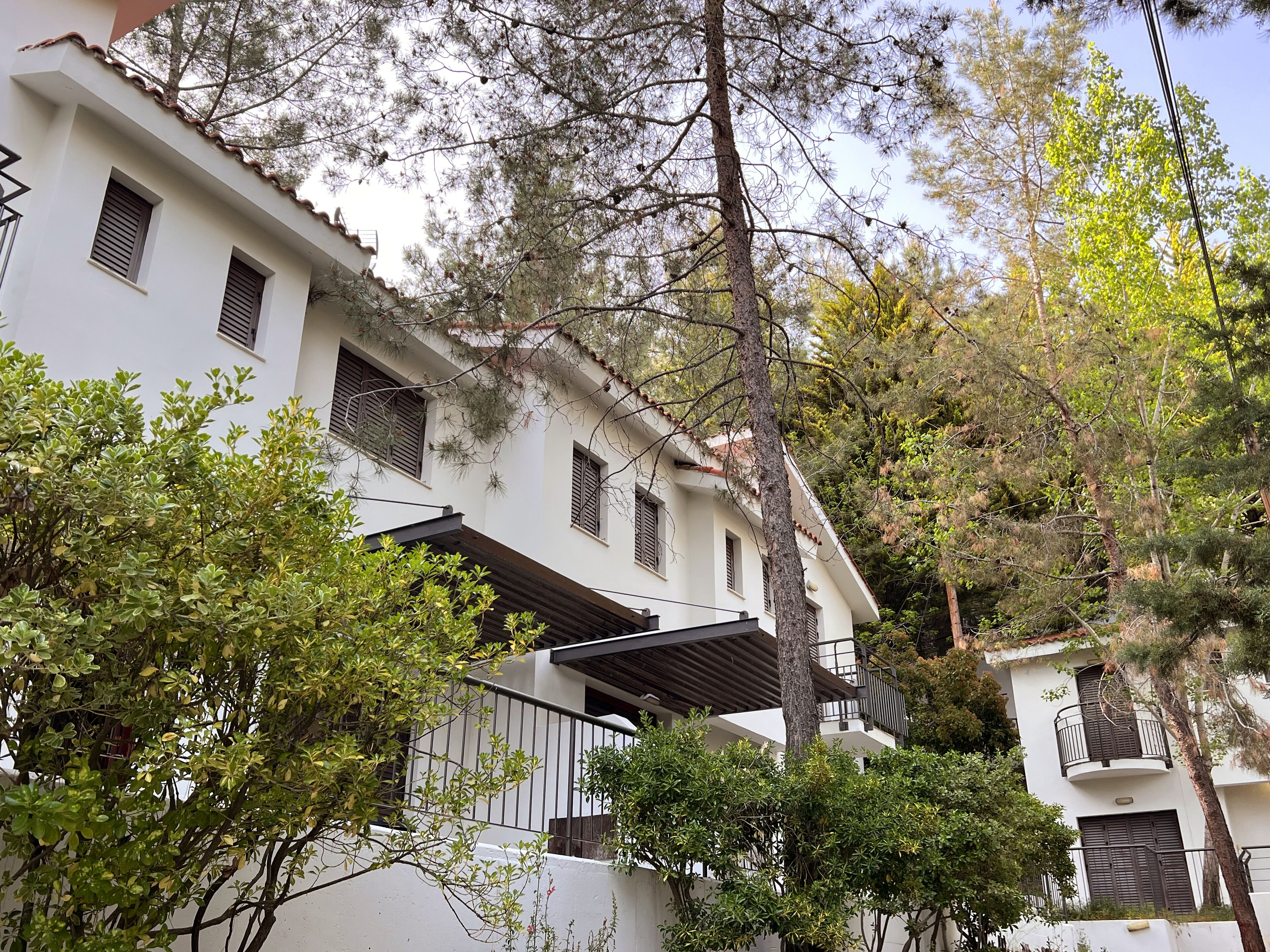Un edificio blanco con numerosas ventanas y balcones, rodeado de árboles y vegetación.
