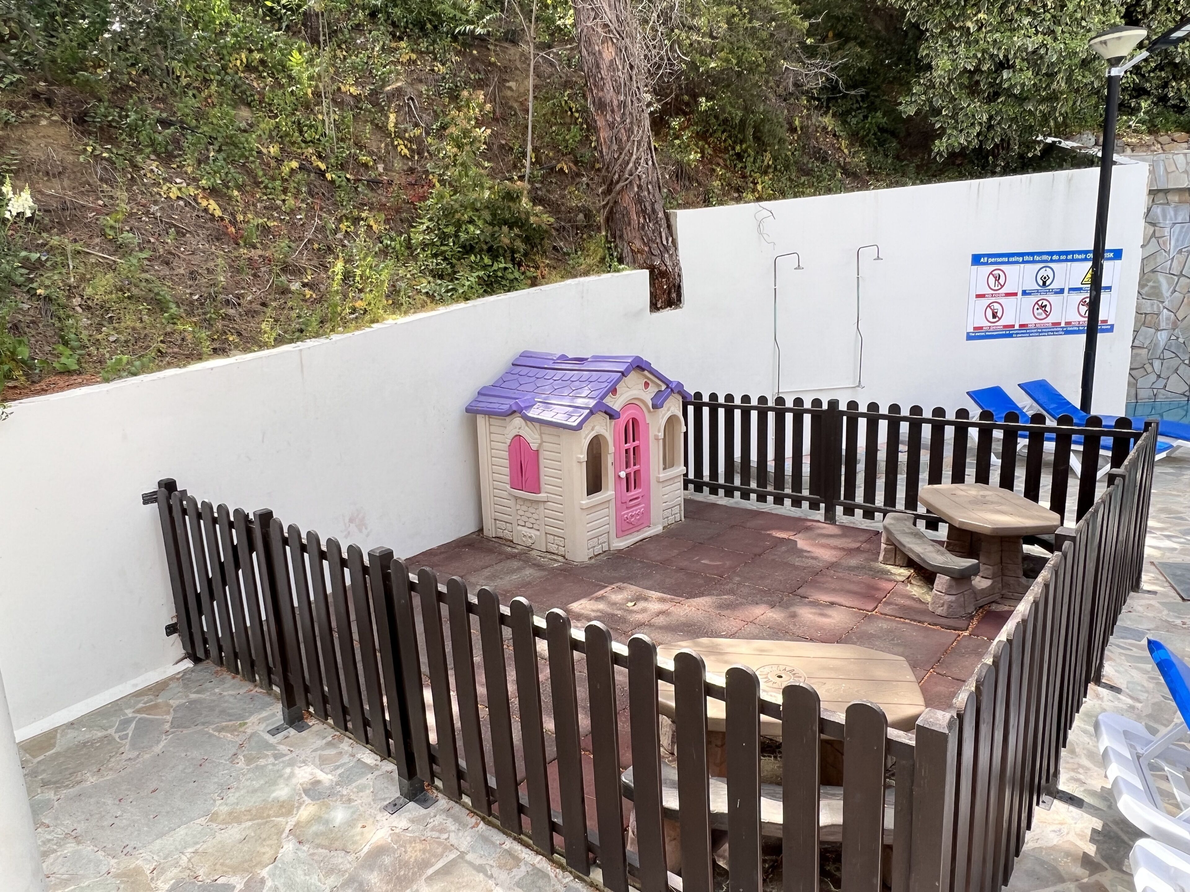 Un área al aire libre cercada con una casita de juegos, una mesa de picnic y un banco.