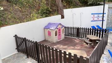 Un área al aire libre cercada con una casita de juegos, una mesa de picnic y un banco.