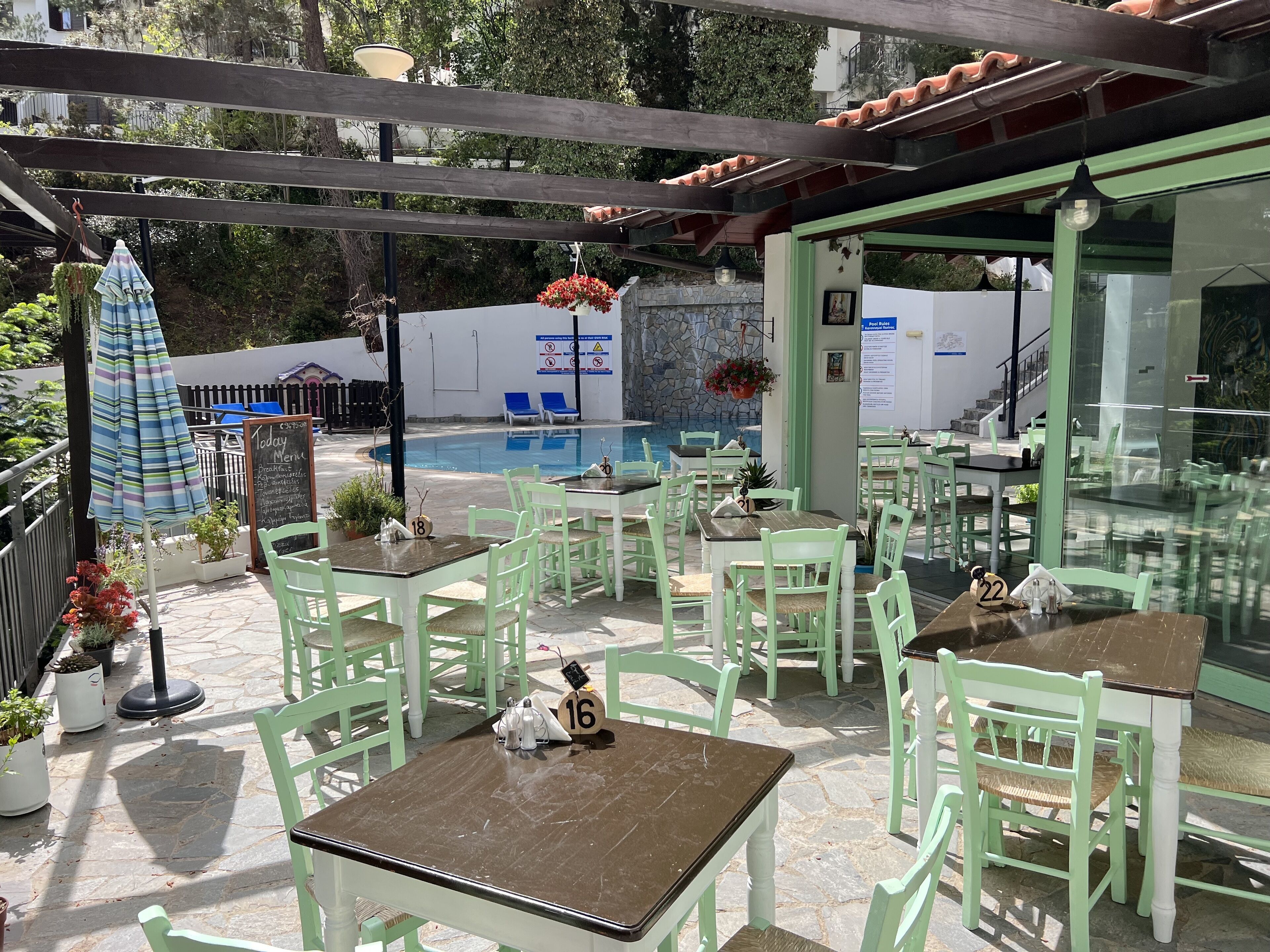 Un espace extérieur aménagé en terrasse, avec des chaises et des tables vertes, une piscine et un mur en pierre.