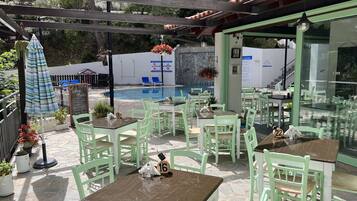 Un espace extérieur aménagé en terrasse, avec des chaises et des tables vertes, une piscine et un mur en pierre.