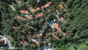 An aerial view of a residential area with multiple houses, a swimming pool, and dense surrounding trees. - Poed Residences (Platres)