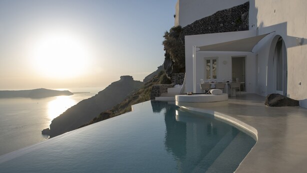 Una piscina infinita moderna con vista al mar y un edificio blanco de fachada de piedra.