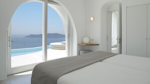 Un dormitorio con un amplio ventanal de arco, una cama, una mesita de noche y vistas al océano.