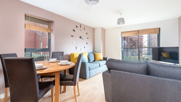 A modern living room with a dining table, grey sofa, and a blue couch. - Bouverie Apartment (Leeds)