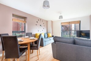 A modern living room with a dining table, grey sofa, and a blue couch. - Bouverie Apartment (Leeds)