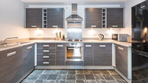 A modern kitchen with dark wood cabinets, a stainless steel range hood, and a built-in oven. - Bouverie Apartment (Leeds)