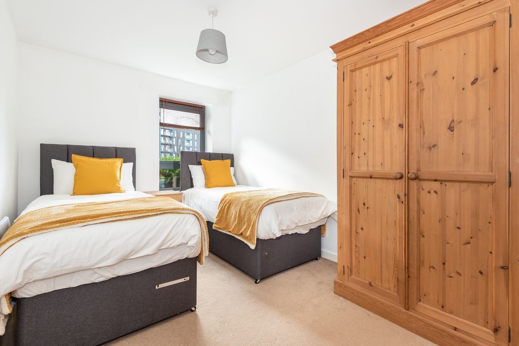A bedroom with two beds, a wardrobe, and a window with blinds.