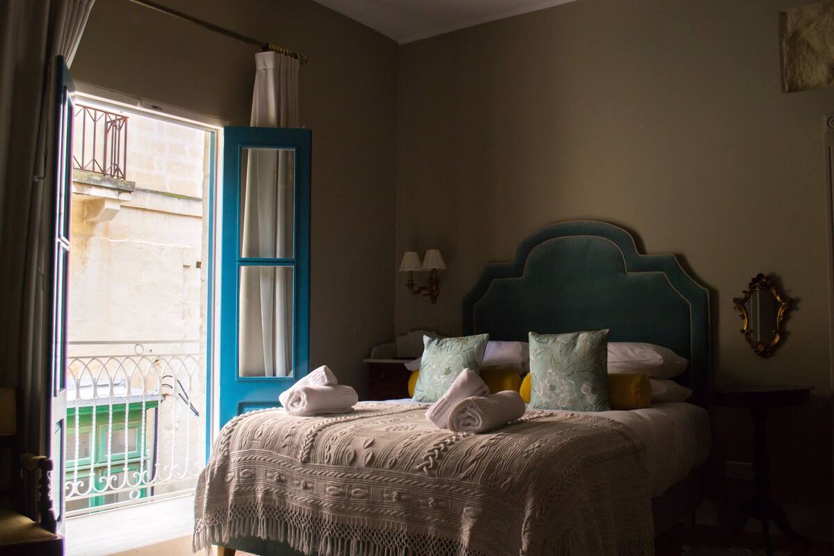 Un dormitorio con cama, ventana con vistas, puerta y mesita de noche con lámparas.