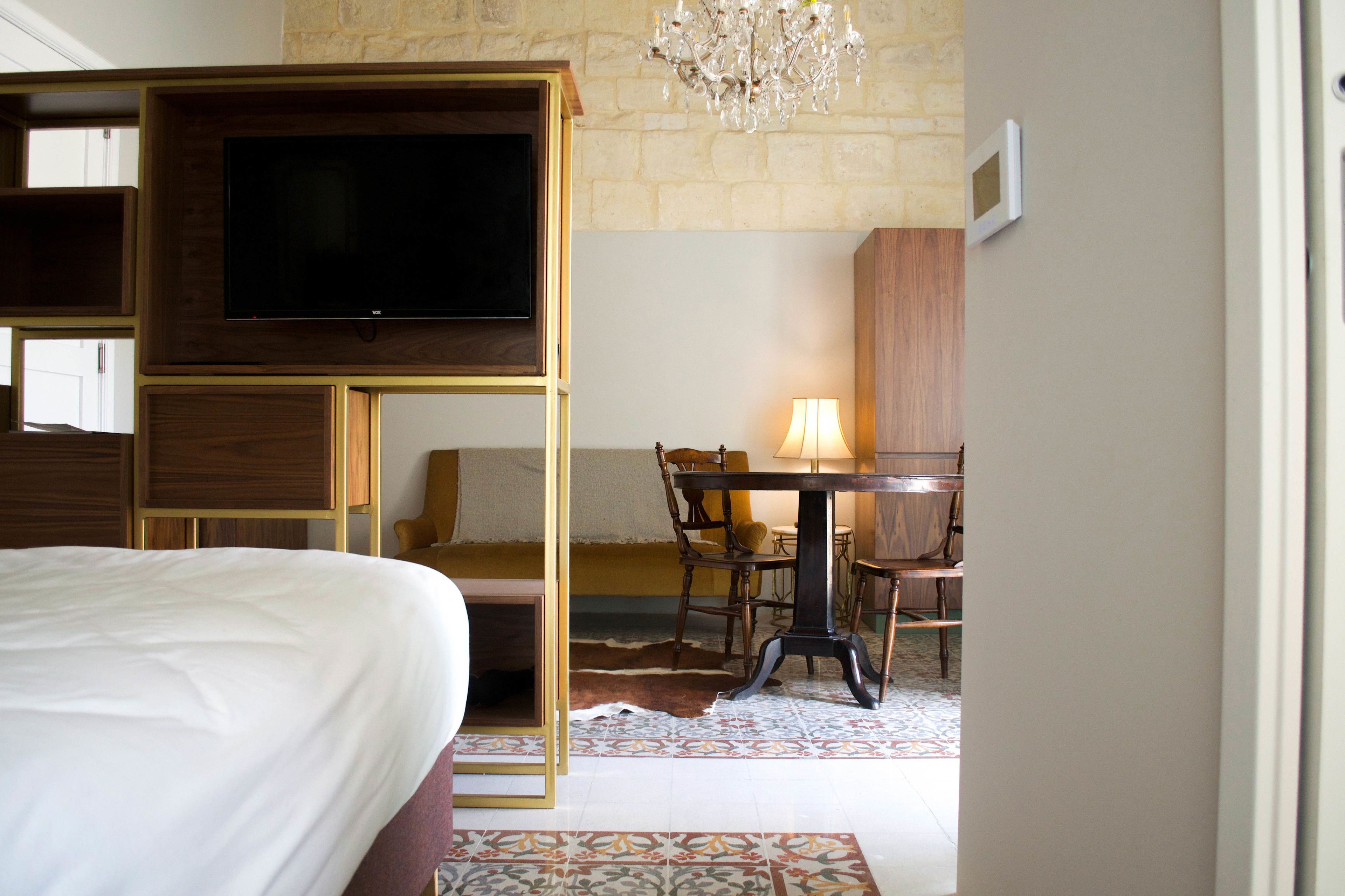 Une chambre d’hôtel comprenant un lit, un téléviseur fixé sur un panneau en bois, une table à manger avec des chaises et un lustre.