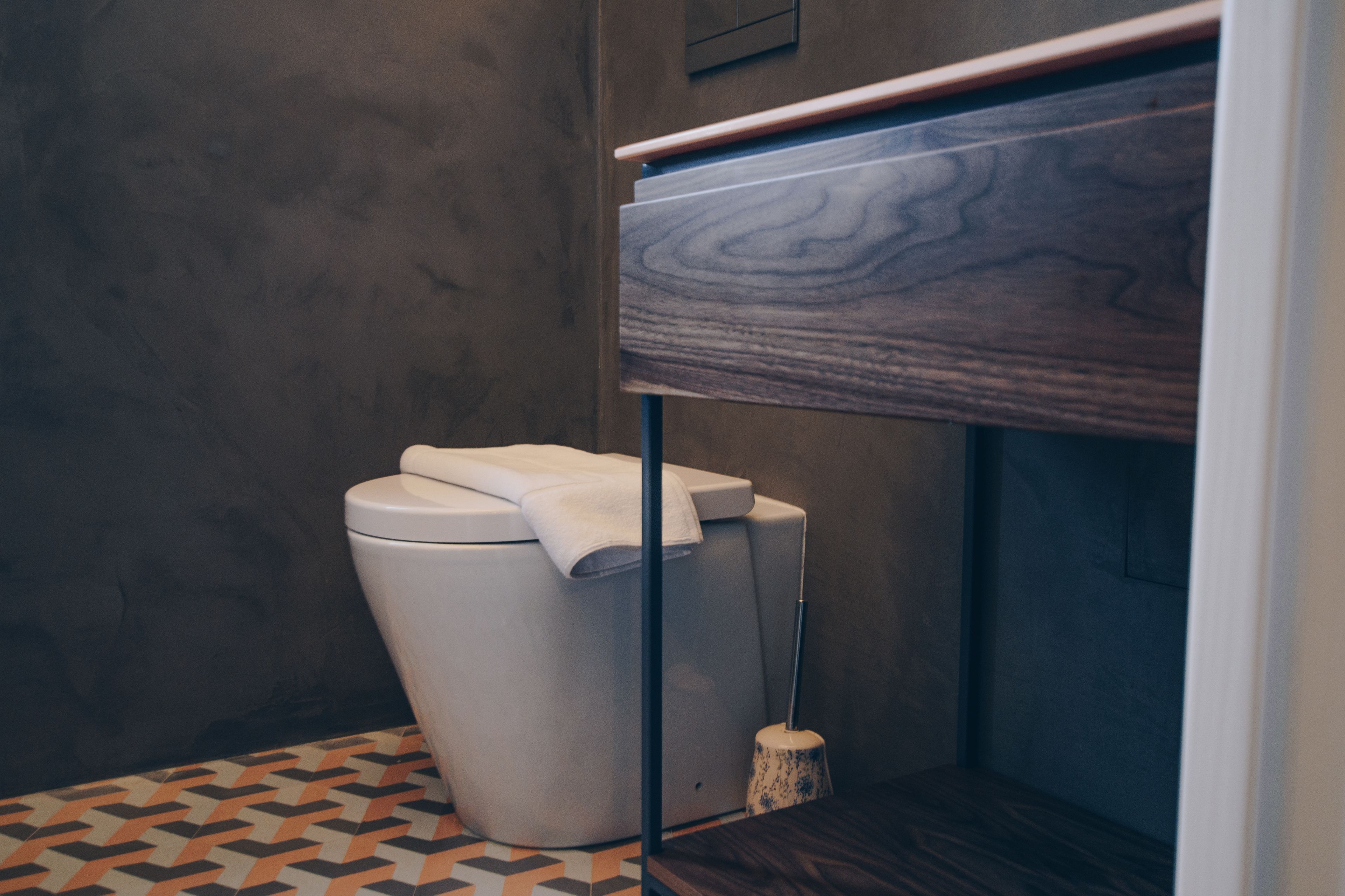 A modern bathroom with a toilet, a wooden vanity, and a patterned floor.