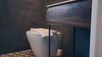 A modern bathroom with a toilet, a wooden vanity, and a patterned floor.