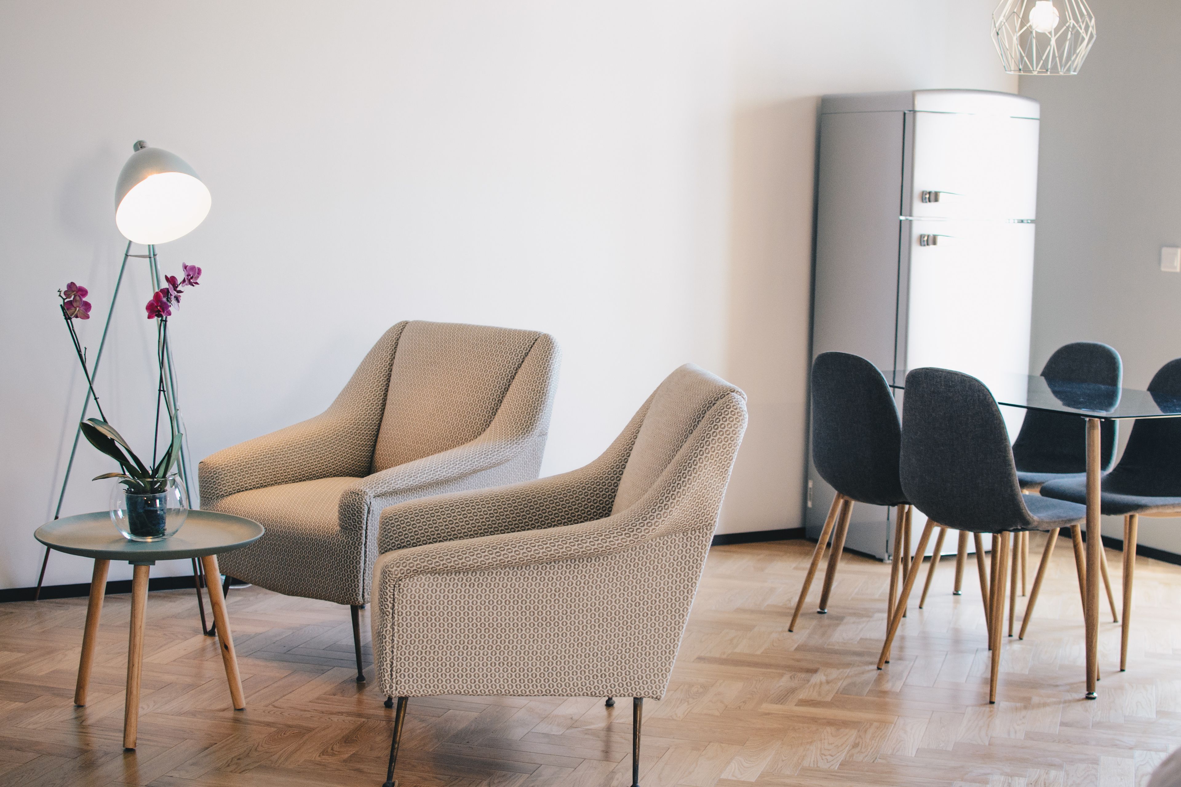 Una habitación moderna con dos sillones color beige, una mesita redonda con una planta en maceta, y una mesa de comedor con cubierta de vidrio y sillas.