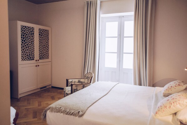 A bedroom with a bed, a chair, a wardrobe, and a window with curtains. - Sally Port Suites (Valletta)