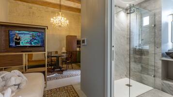 Ein modernes Hotelzimmer mit Fernseher, einer in Glas abgeschirmten Dusche, Holzboden und einem Kronleuchter.