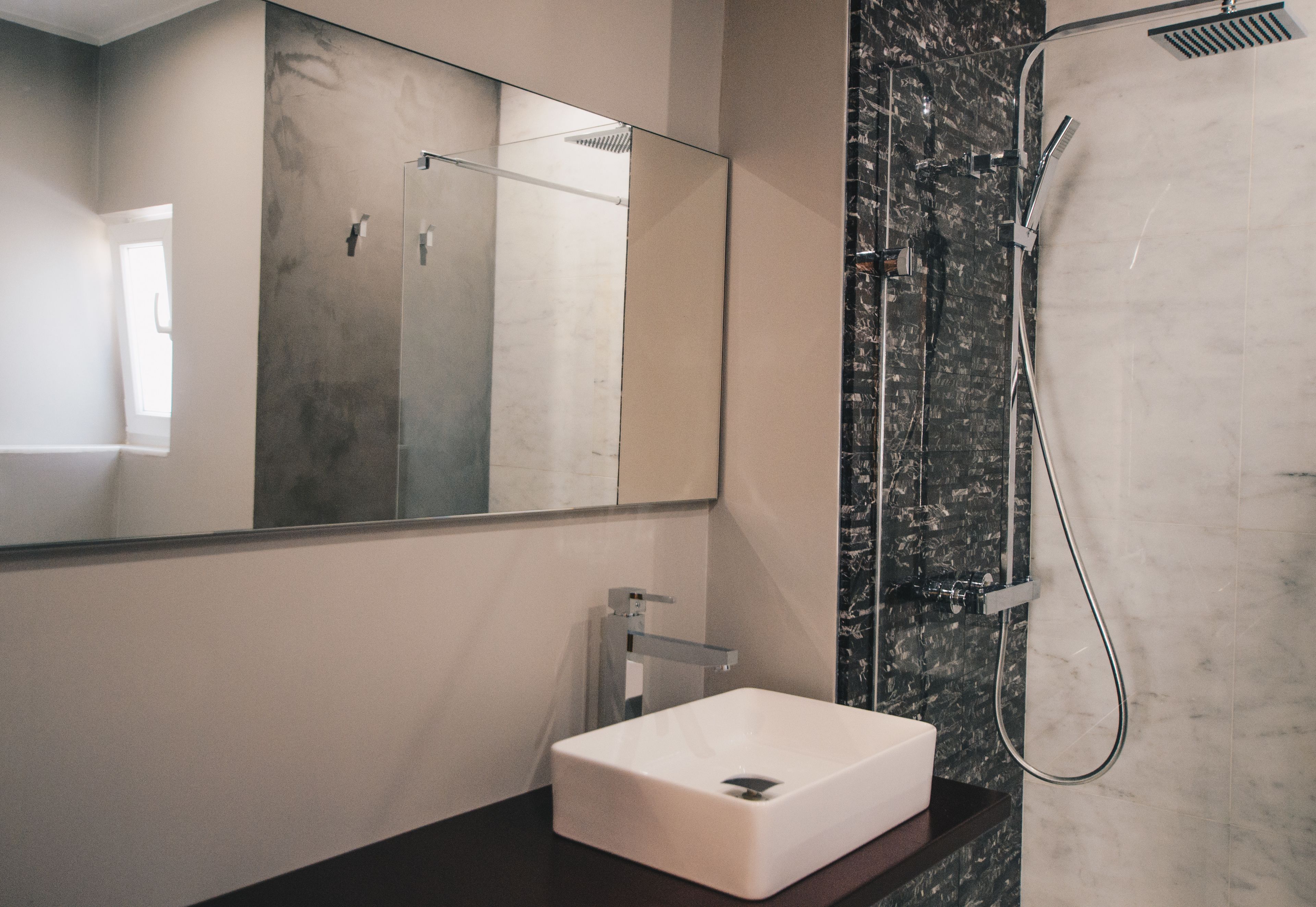 Un bany modern amb un mirall gran, un lavabo blanc i una dutxa amb plat de boira.