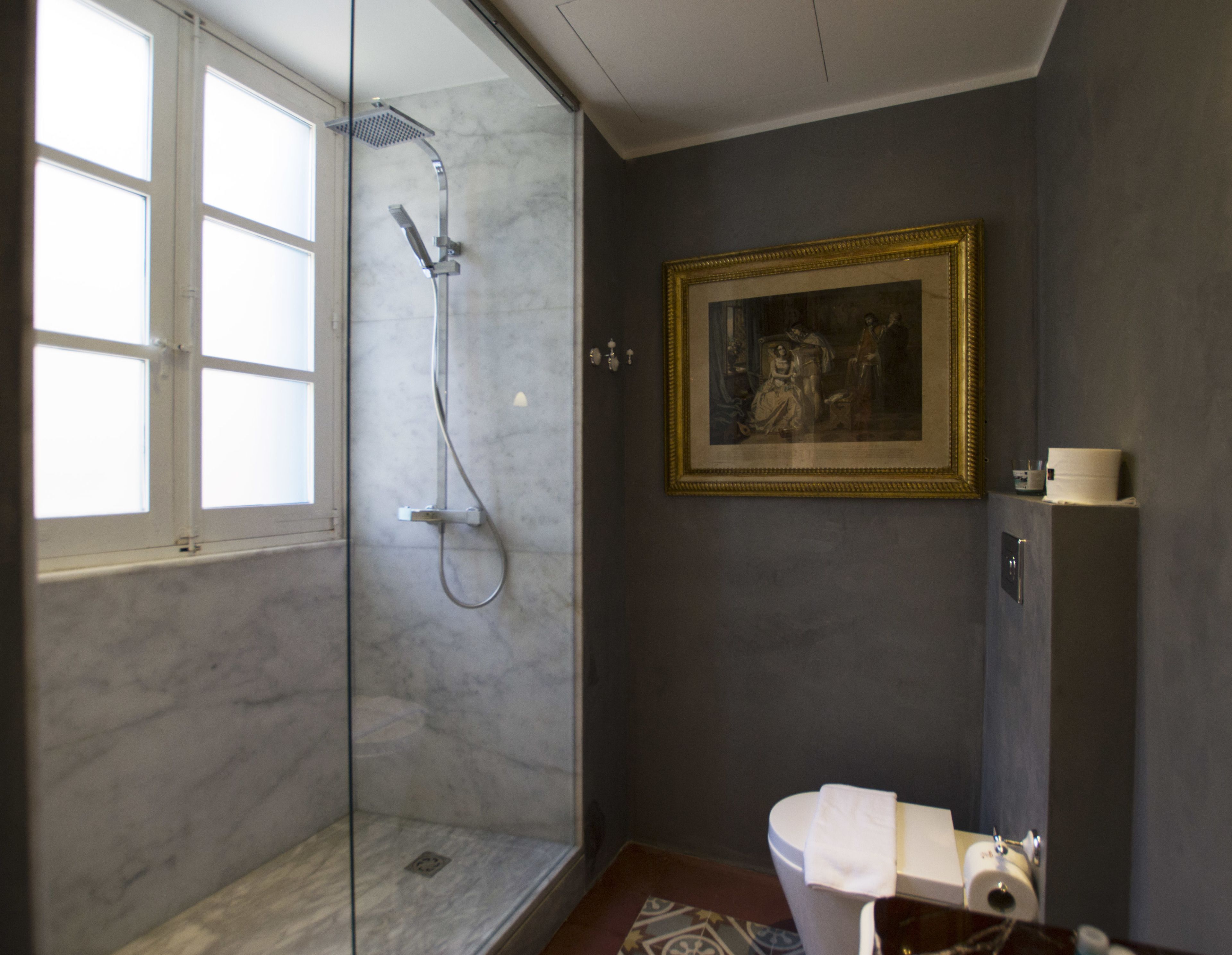 A bathroom with a glass shower enclosure, a toilet with a towel, and a framed painting on the wall.