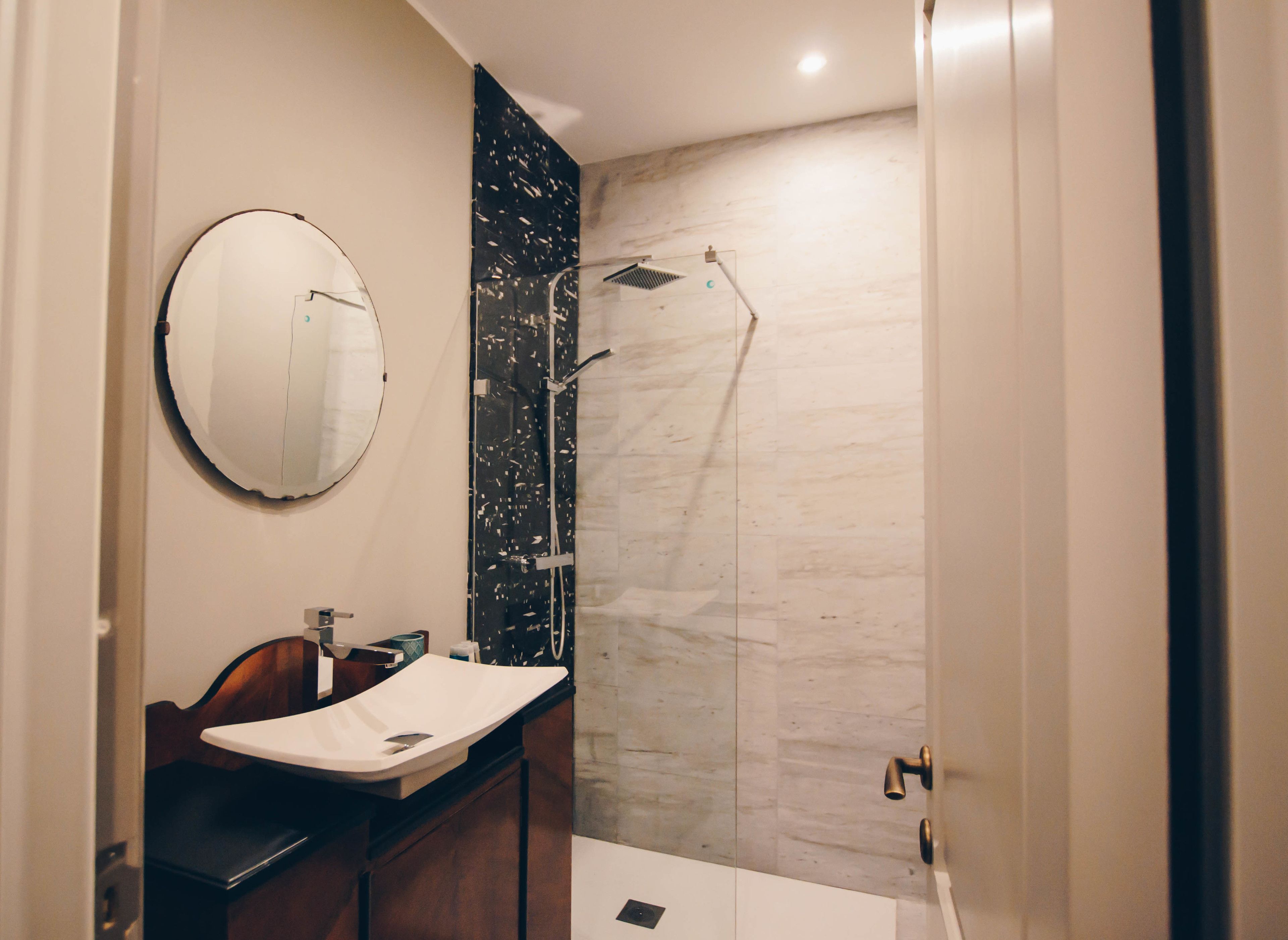 Une salle de bain moderne avec un grand miroir rond, un meuble-lavabo en bois et une douche à parois de verre.