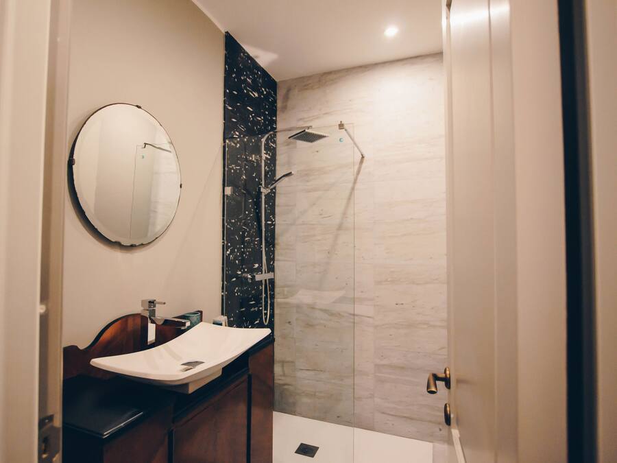 Une salle de bain moderne avec un grand miroir rond, un meuble-lavabo en bois et une douche à parois de verre.