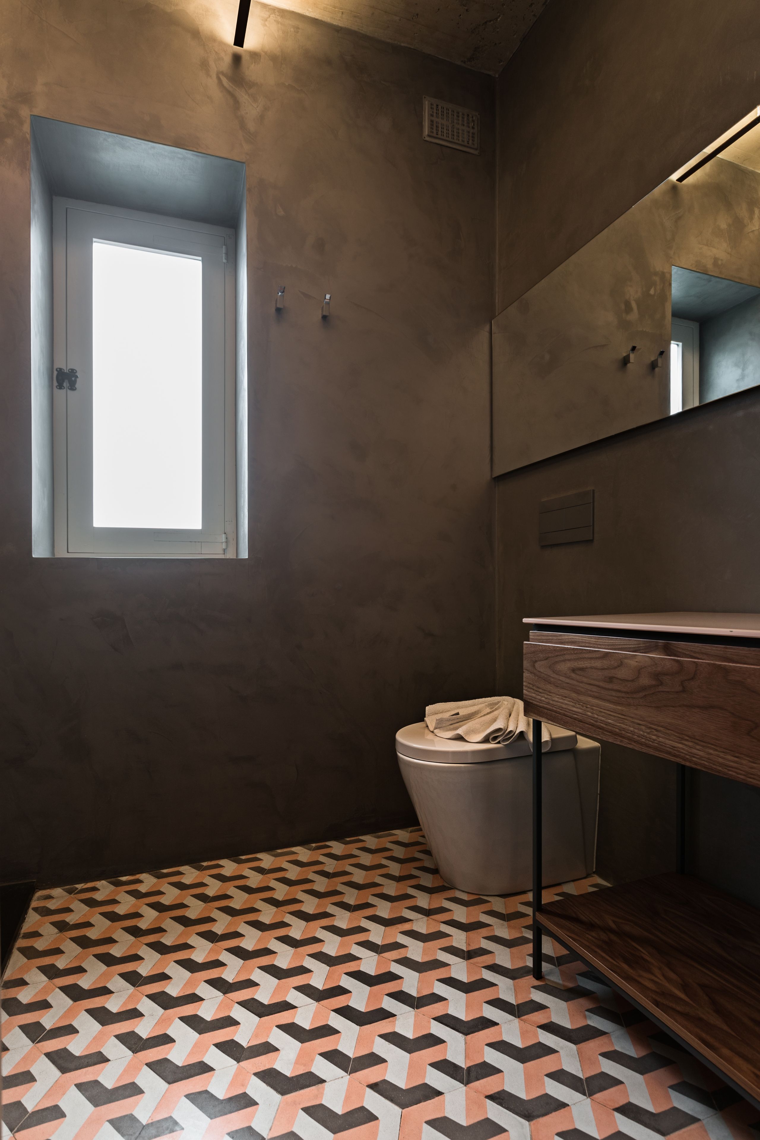 Un baño con suelo de estampado geométrico, una ventana, un espejo y un estante de madera.