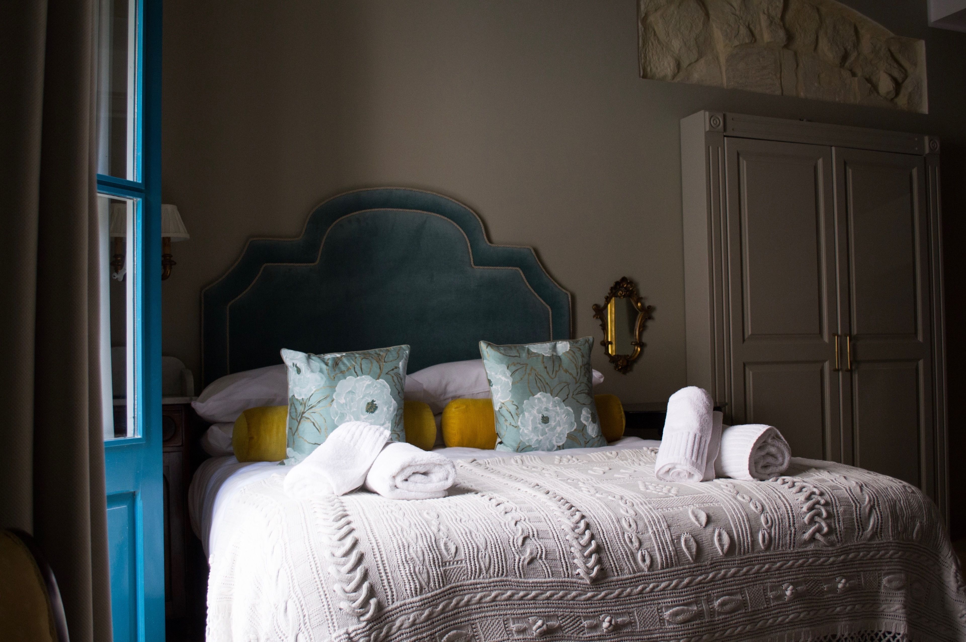 A neatly made bed with a patterned bedspread, pillows, and rolled towels.