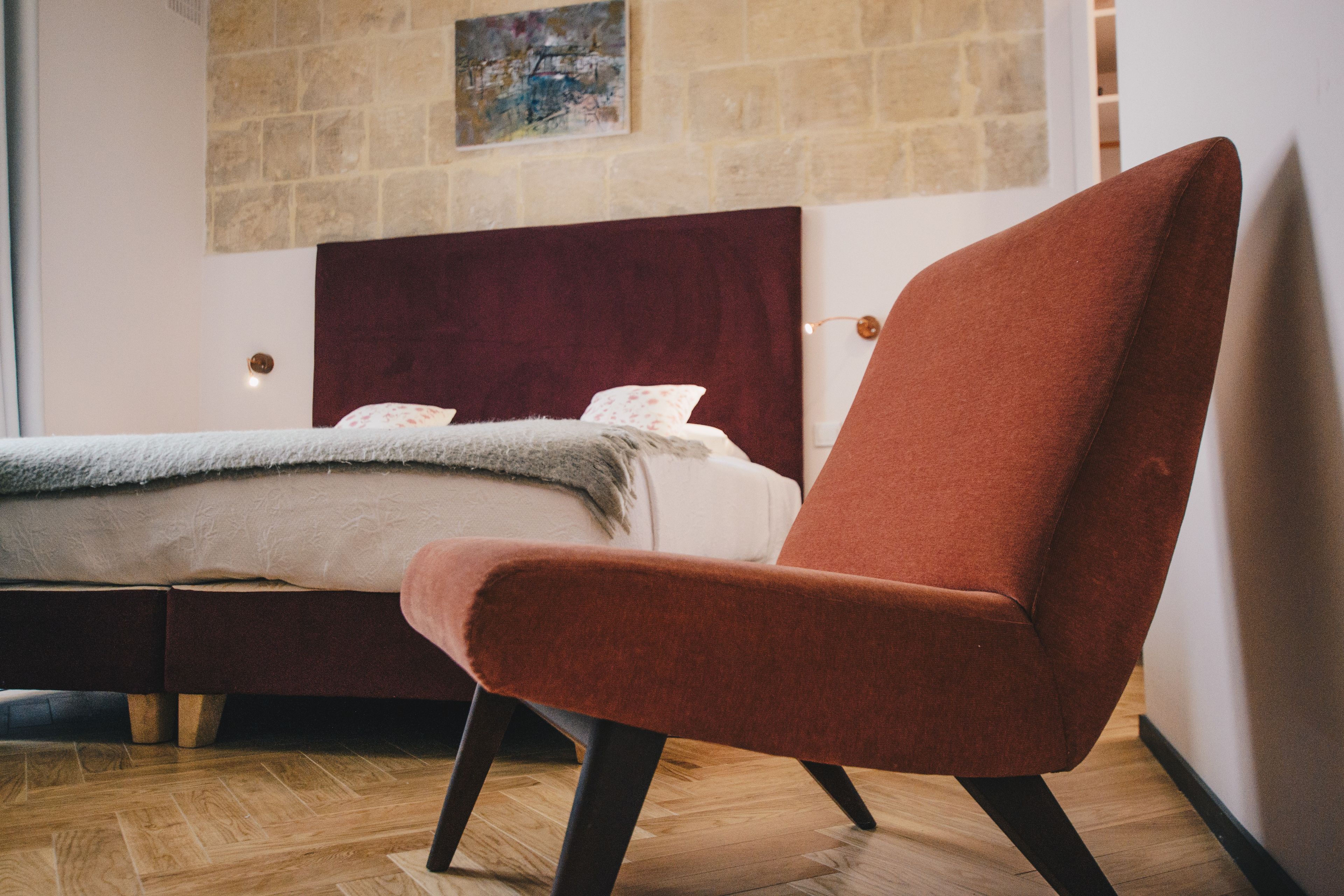 A modern bedroom with a large bed, a red armchair, and a wooden floor.