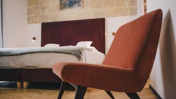 A modern bedroom with a large bed, a red armchair, and a wooden floor.