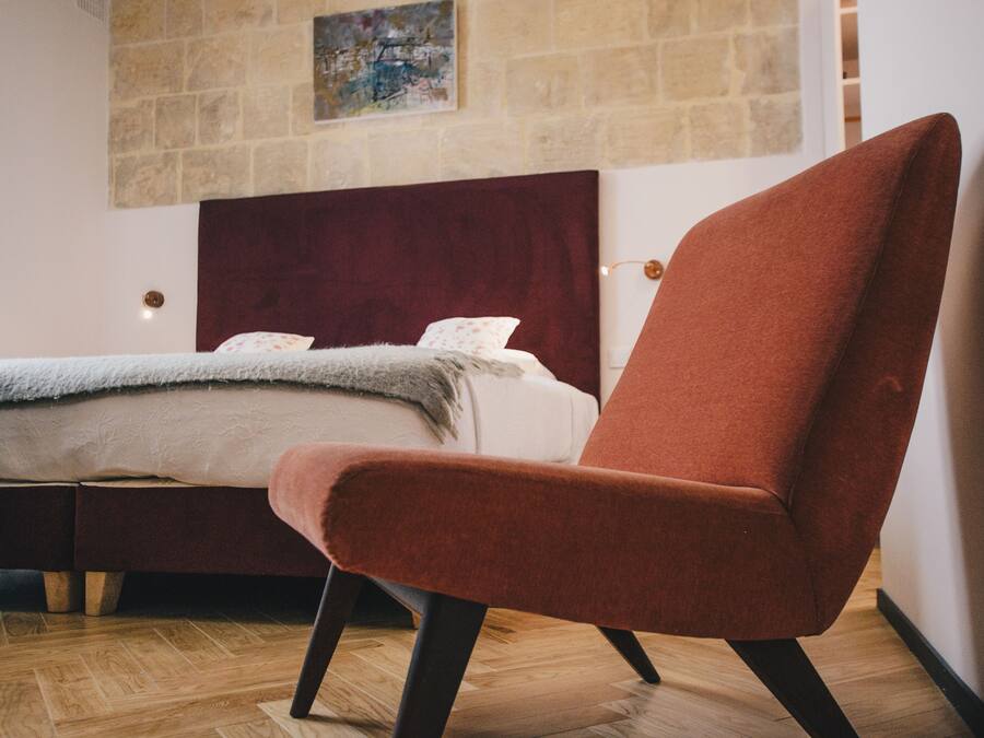 A modern bedroom with a large bed, a red armchair, and a wooden floor.