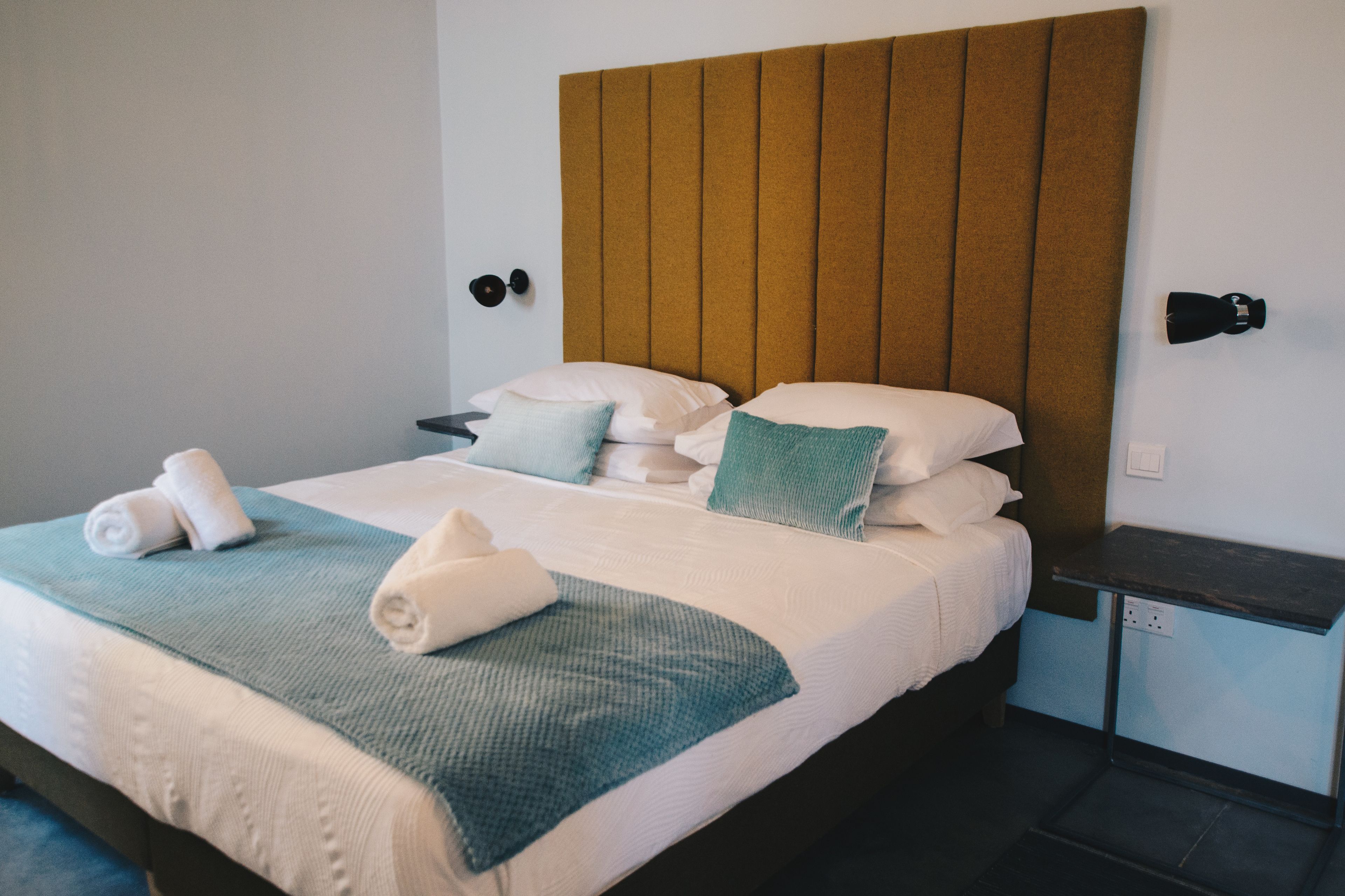 A neatly made bed with a blue and white bedspread, pillows, and rolled towels.