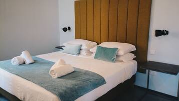 A neatly made bed with a blue and white bedspread, pillows, and rolled towels.