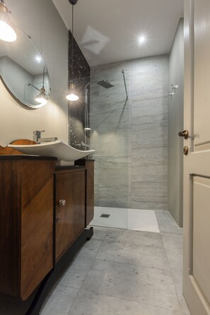 Un baño moderno con tocador de madera, un espejo grande y zona de ducha.