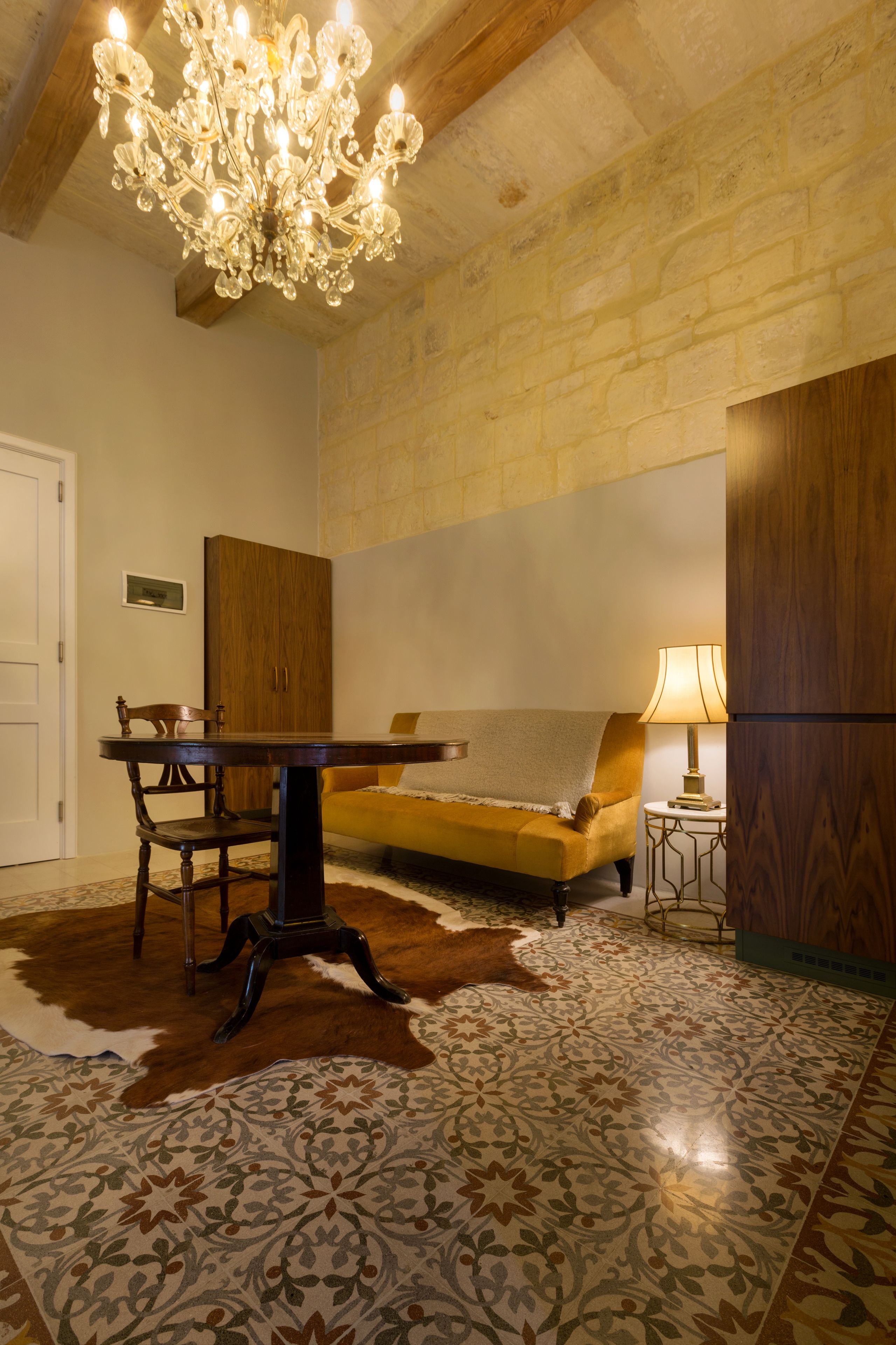 Une pièce avec un lustre, un canapé, un meuble en bois et un tapis à motifs.