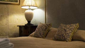 Un lit bien fait, recouvert d’une couverture beige et agrémenté de deux coussins à motifs, une lampe de chevet et un tableau encadré au mur.