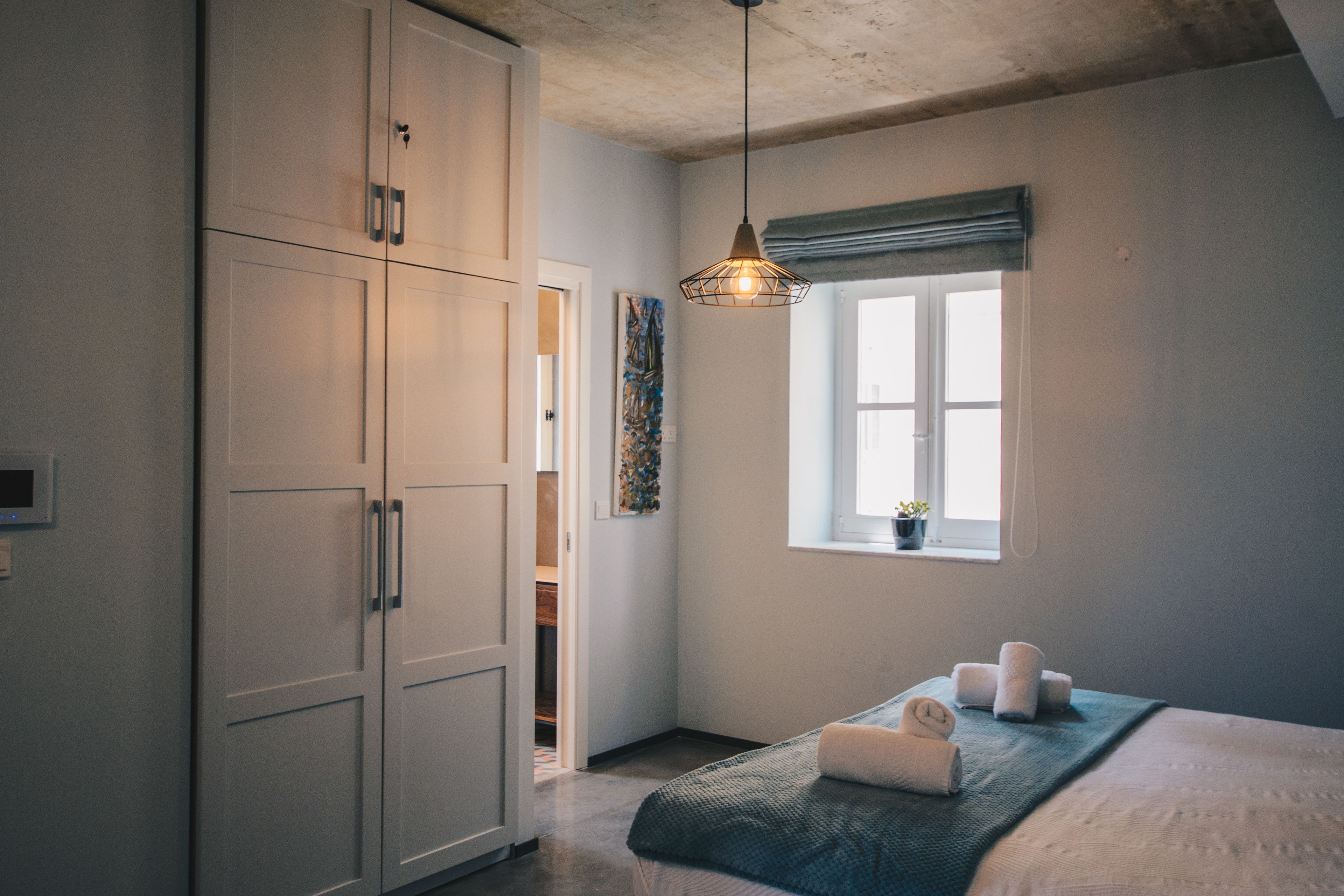 Ein Schlafzimmer mit Bett, Kleiderschrank, Fenster mit Aussicht und einer Pendelleuchte.