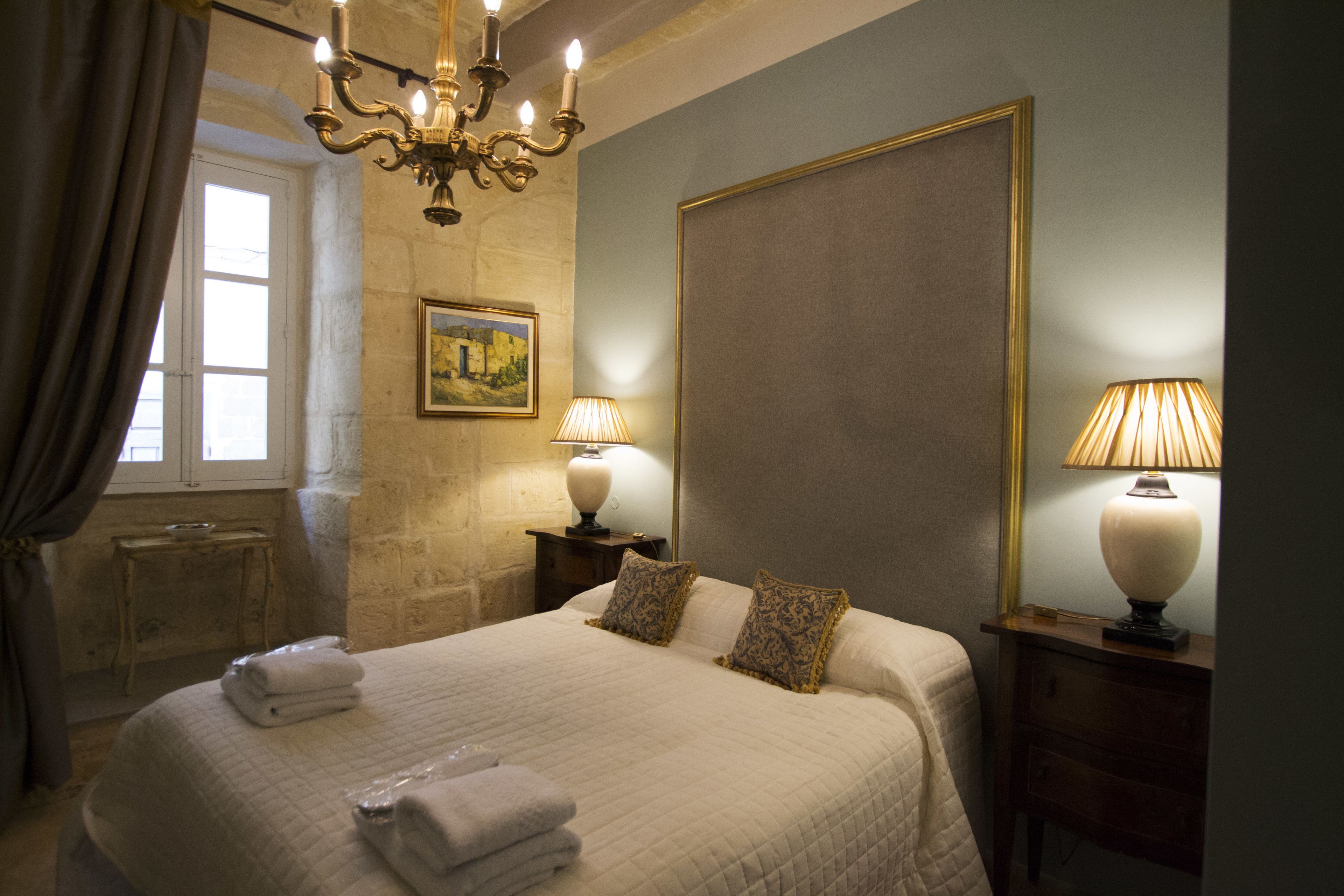 Una cama bien hecha con almohadas, una lámpara de noche y un cuadro en la pared.