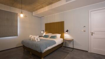 Une chambre à coucher moderne avec une tête de lit en bois, un grand lit recouvert d’une couverture bleue, des lampes de chevet et une porte.