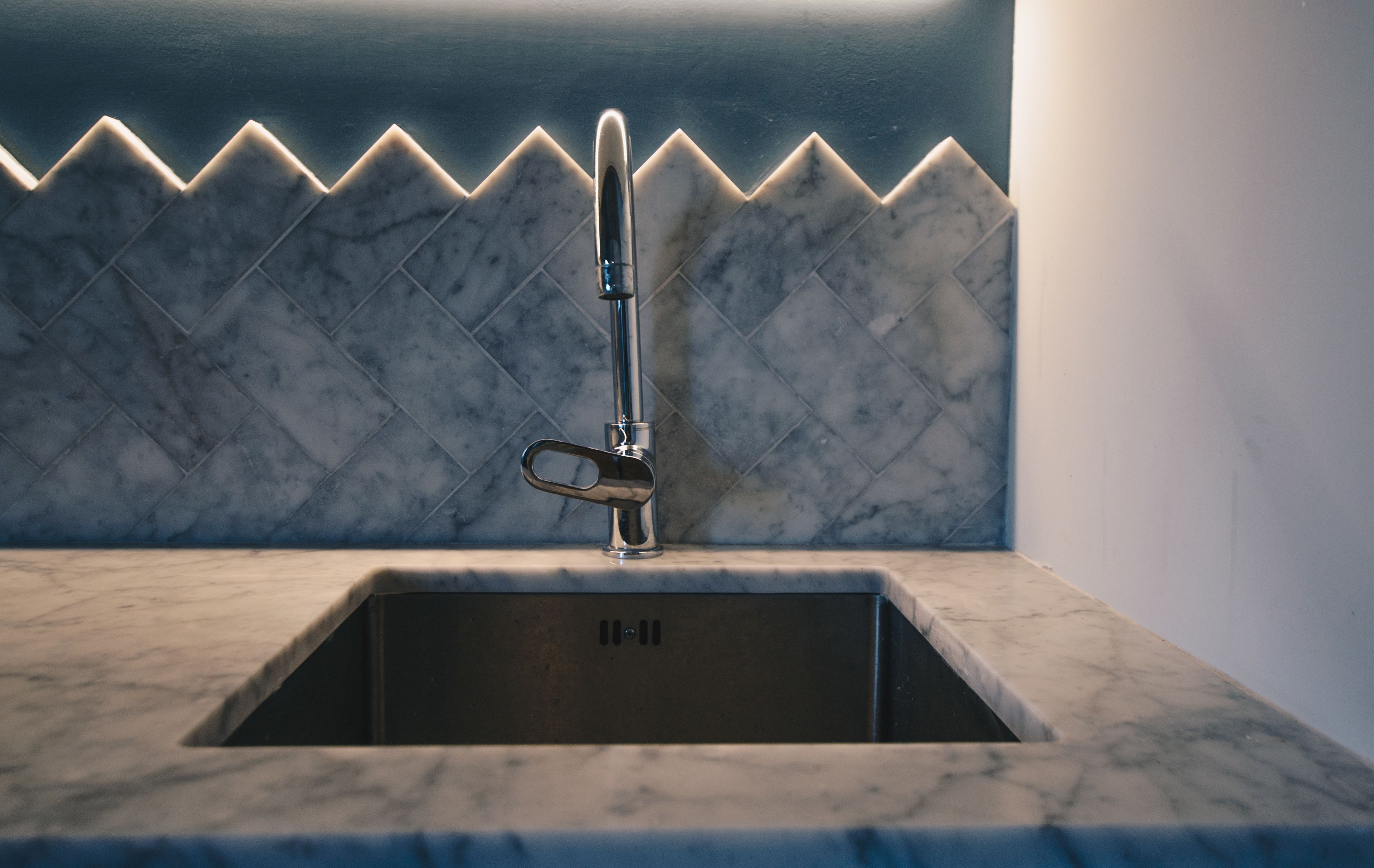 Eine Küchenspüle mit einem modernen Wasserhahn und einer Rückwand mit Diamantmuster.