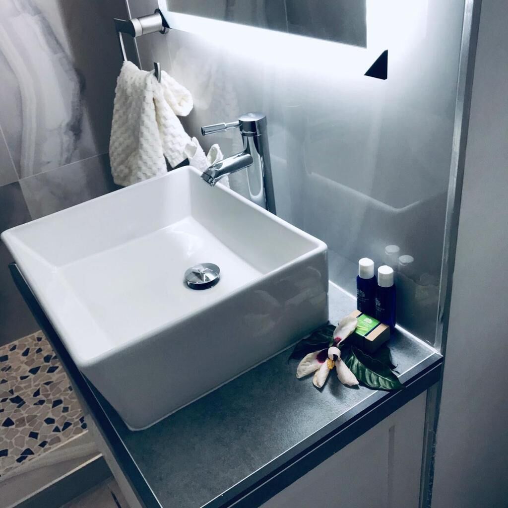 Ein modernes Badezimmer mit einem weißen Waschbecken, einer Handbrause und einer kleinen Ablagefläche für Toilettenartikel.