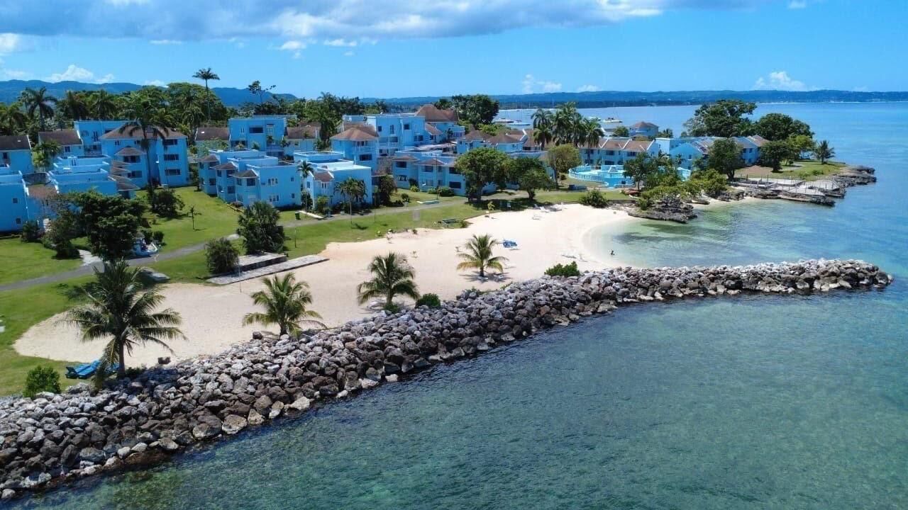 A coastal resort with multiple blue buildings, a sandy beach, and a clear view of the ocean.
