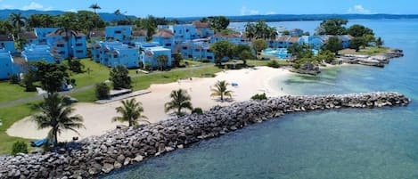 A coastal resort with multiple blue buildings, a sandy beach, and a clear view of the ocean.